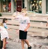 a little boy on lake street playing with a large bubble wand